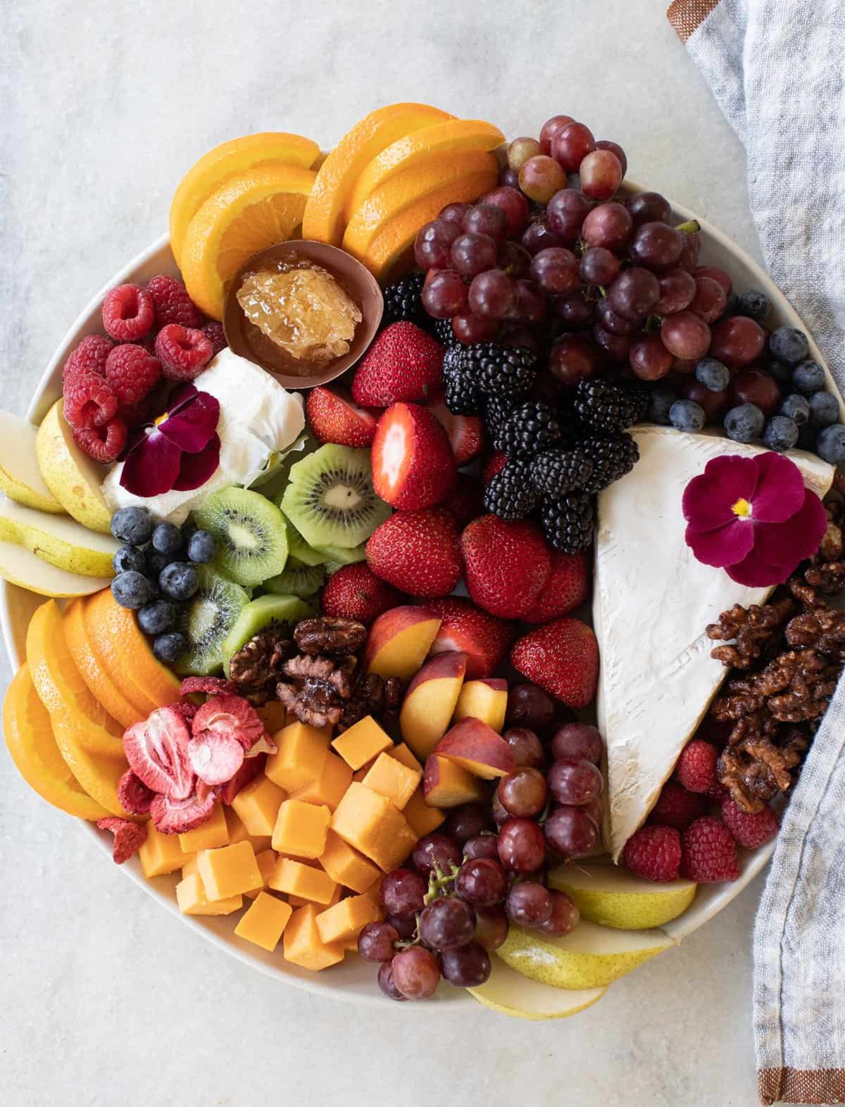 A platter filled with sliced cheese and fresh fruit. 