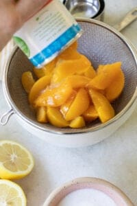 pouring canned peaches into a strainer