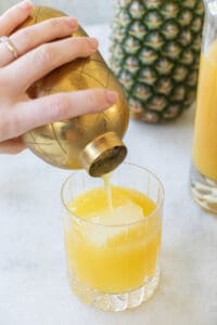 straining a yellow cocktail over ice