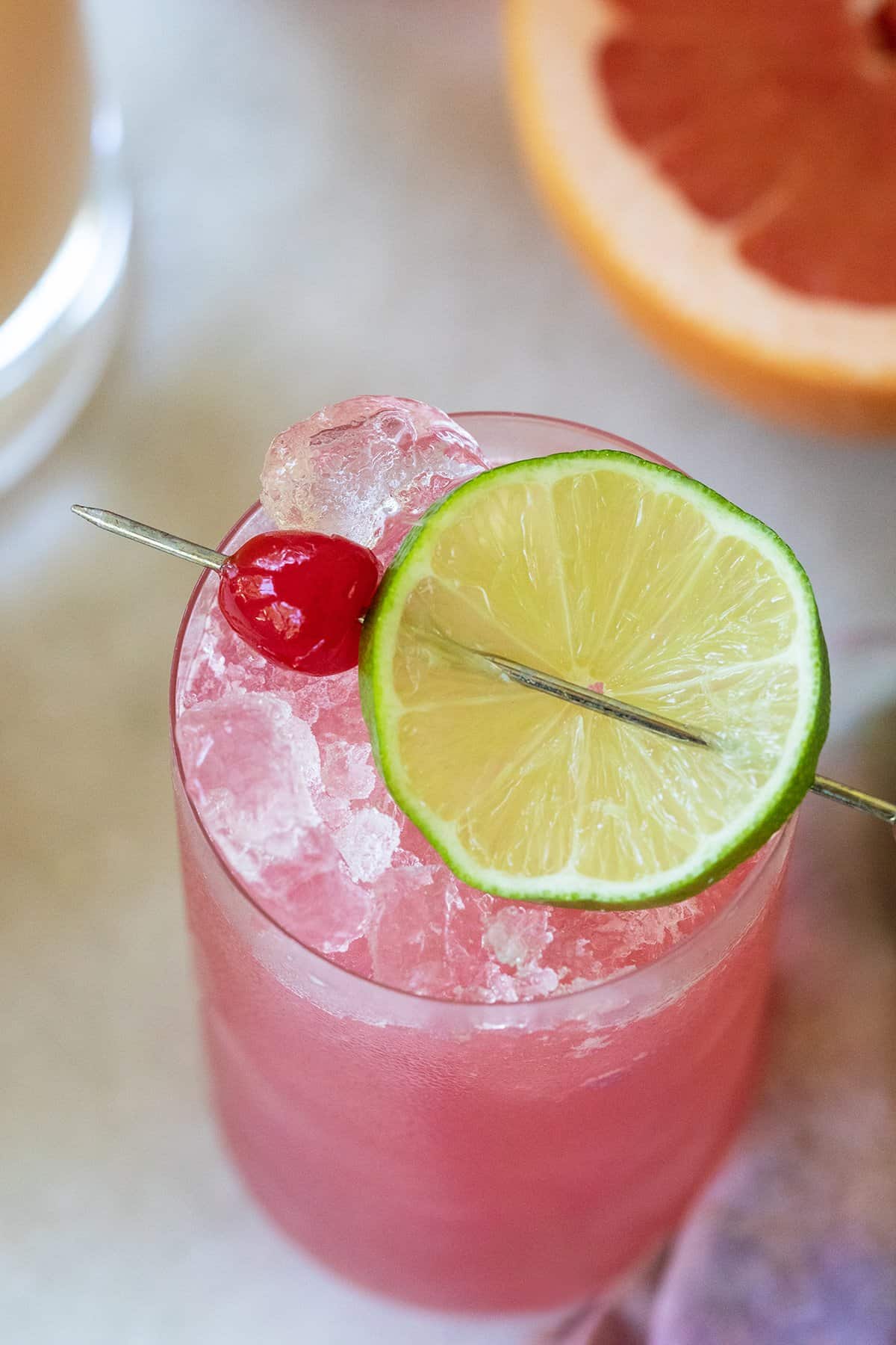 Pink cocktail with lime and cherry garnish.