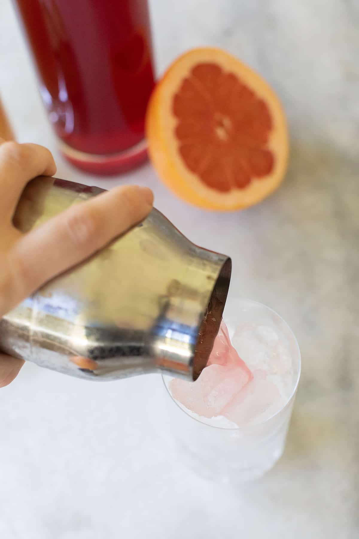 straining a sea breeze cocktail into a tall glass filled with ice