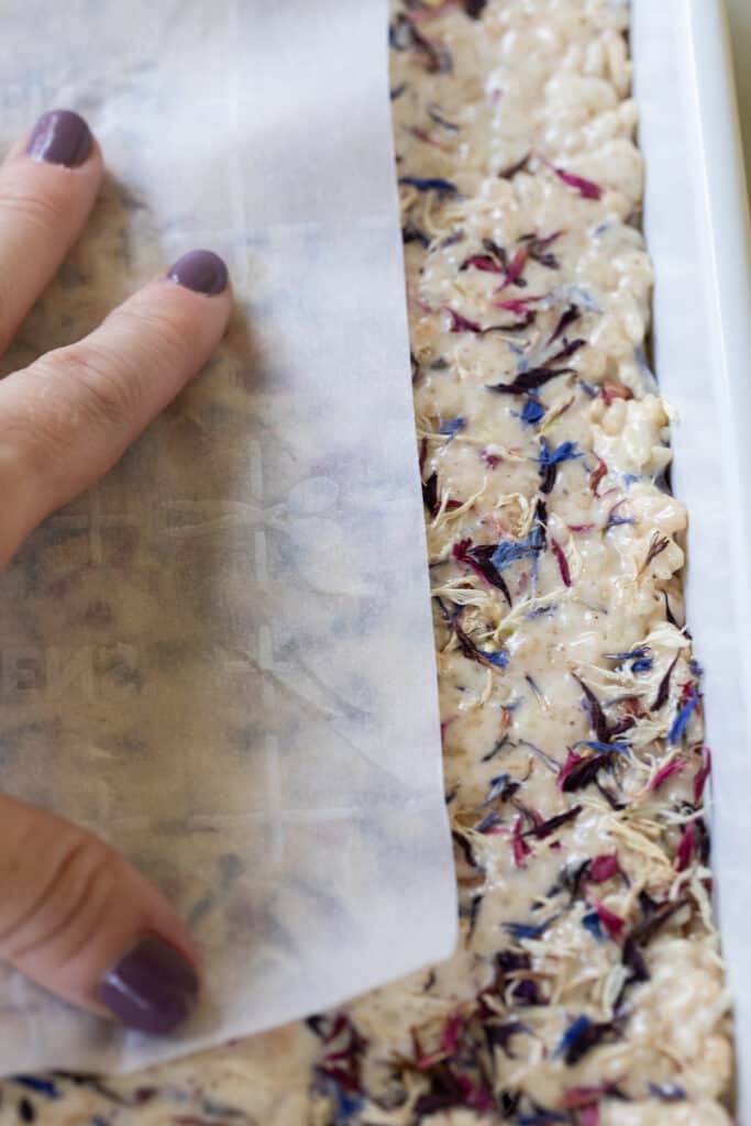 pressing parchment paper down on rice Krispie treat to get an even layer.