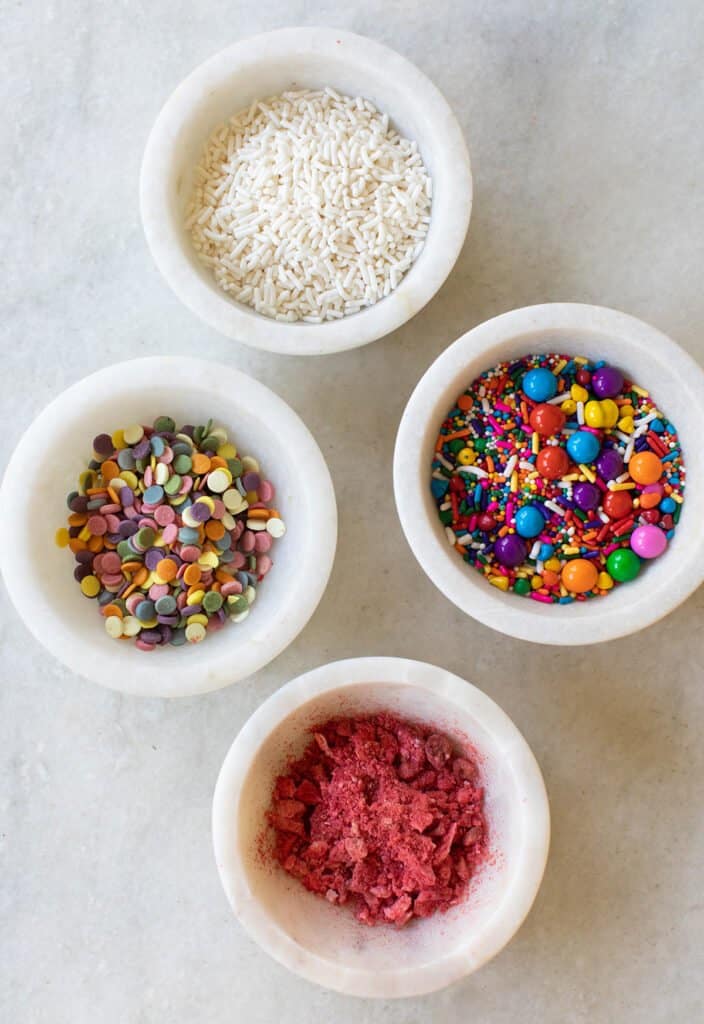 Sprinkles and toppings in bowls to add to pretzel rods.