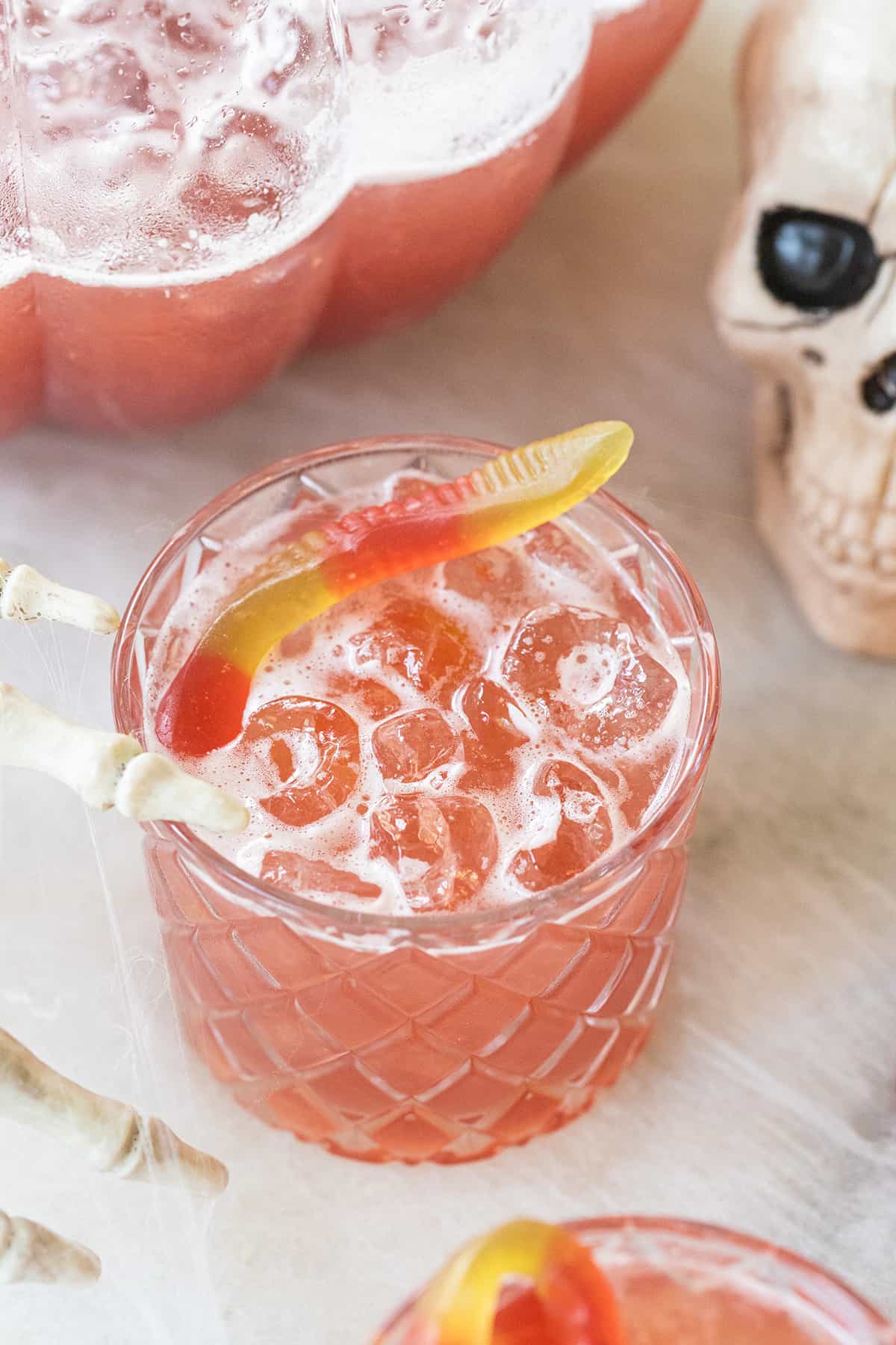 pink drink in a glass with a gummy worm and skeleton hand.