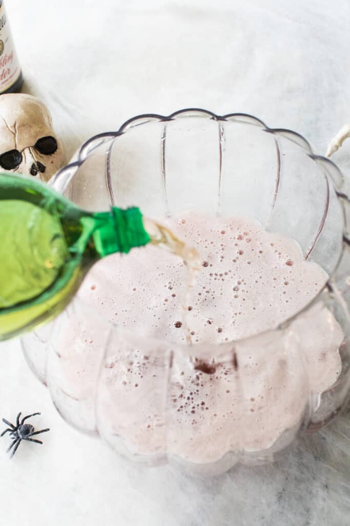 pouring ginger ale into a pumpkin punch bowl