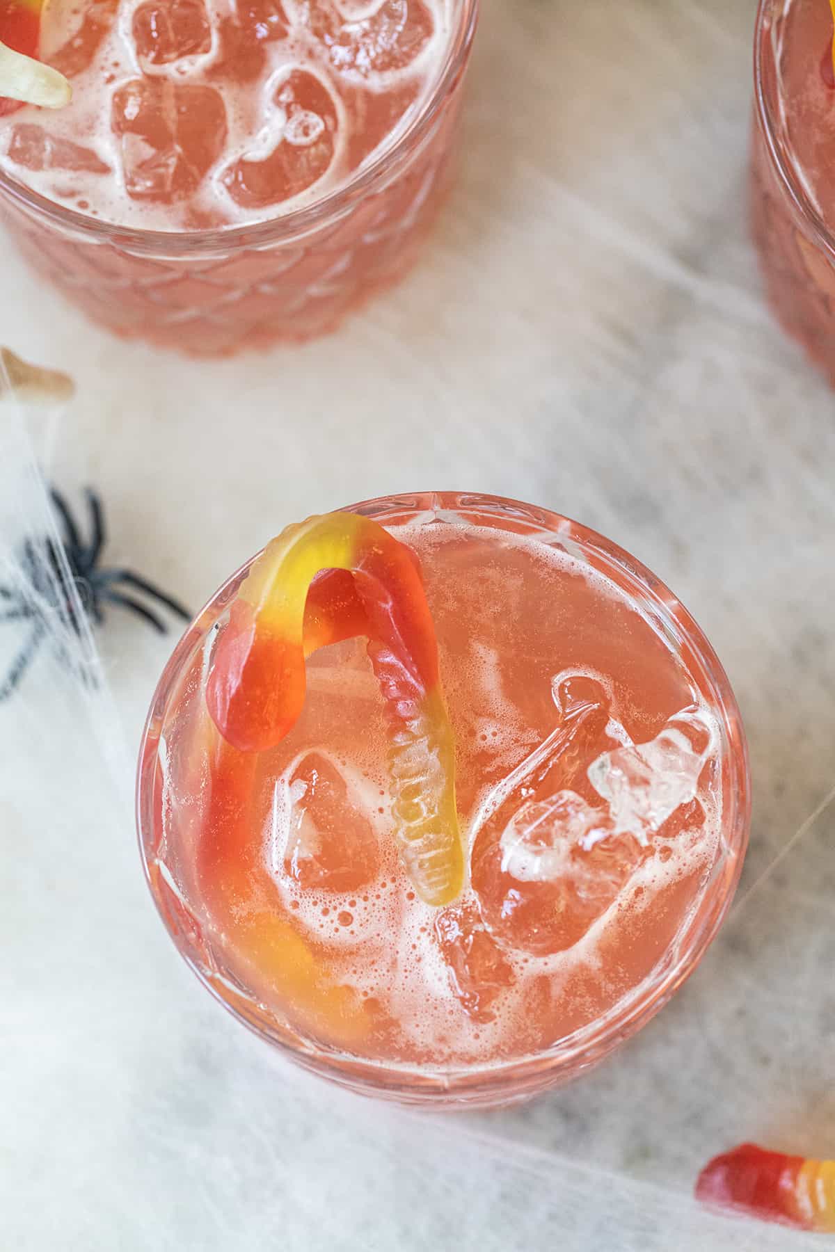 pink cocktail in a glass with ice and a gummy worm.