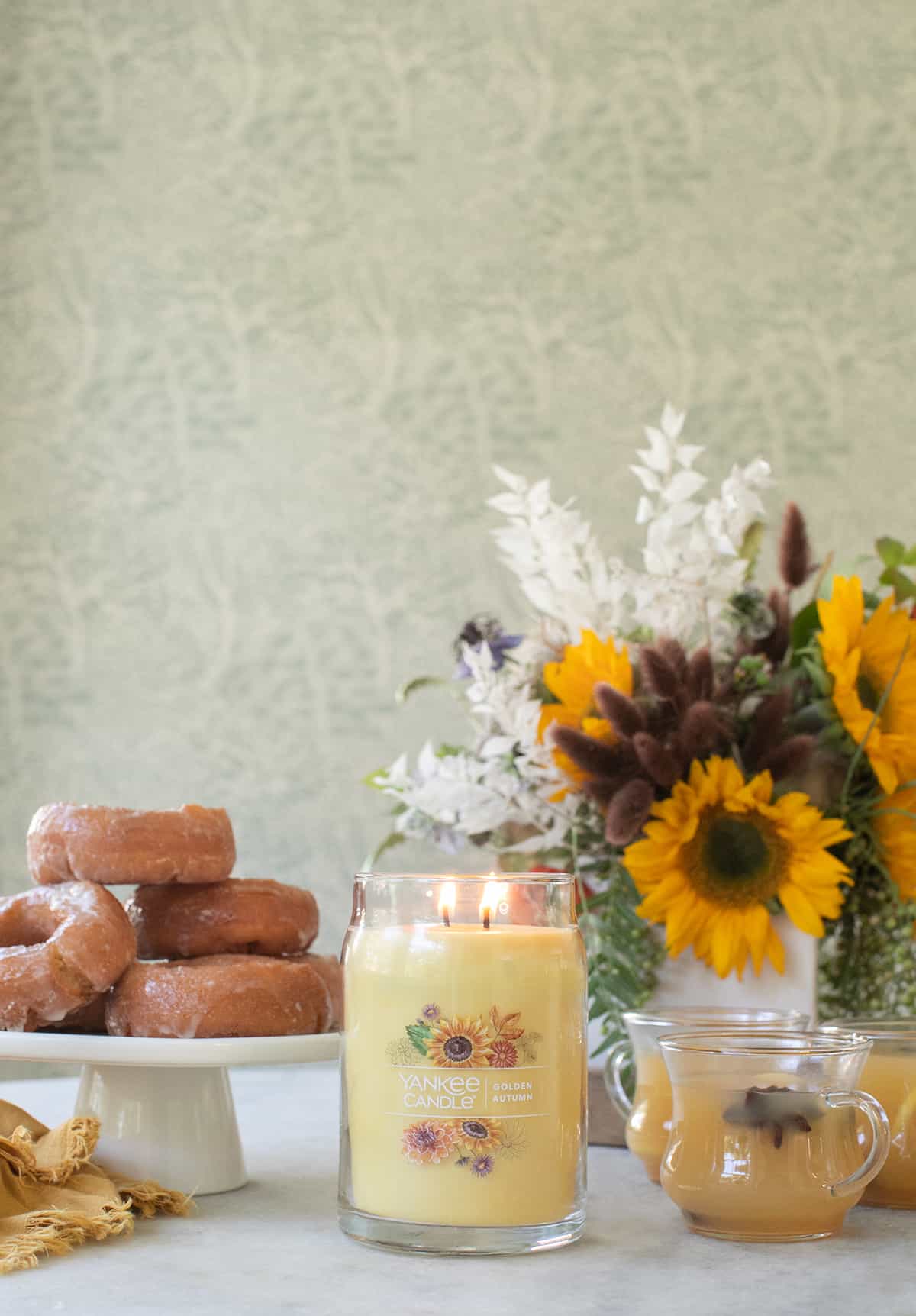 Fall Yankee Candle on a table with sunflowers and apple cider donuts