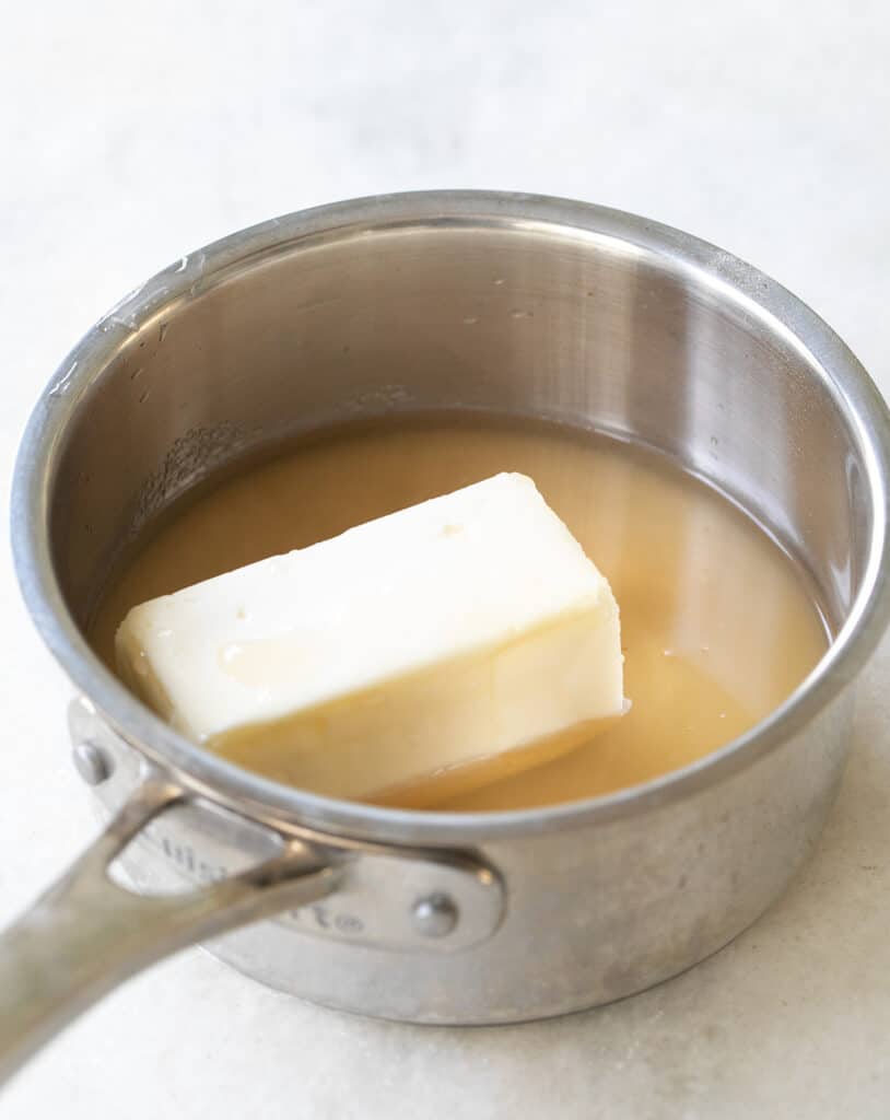 Melting butter and apple cider in a saucepan to make an apple cider glaze.