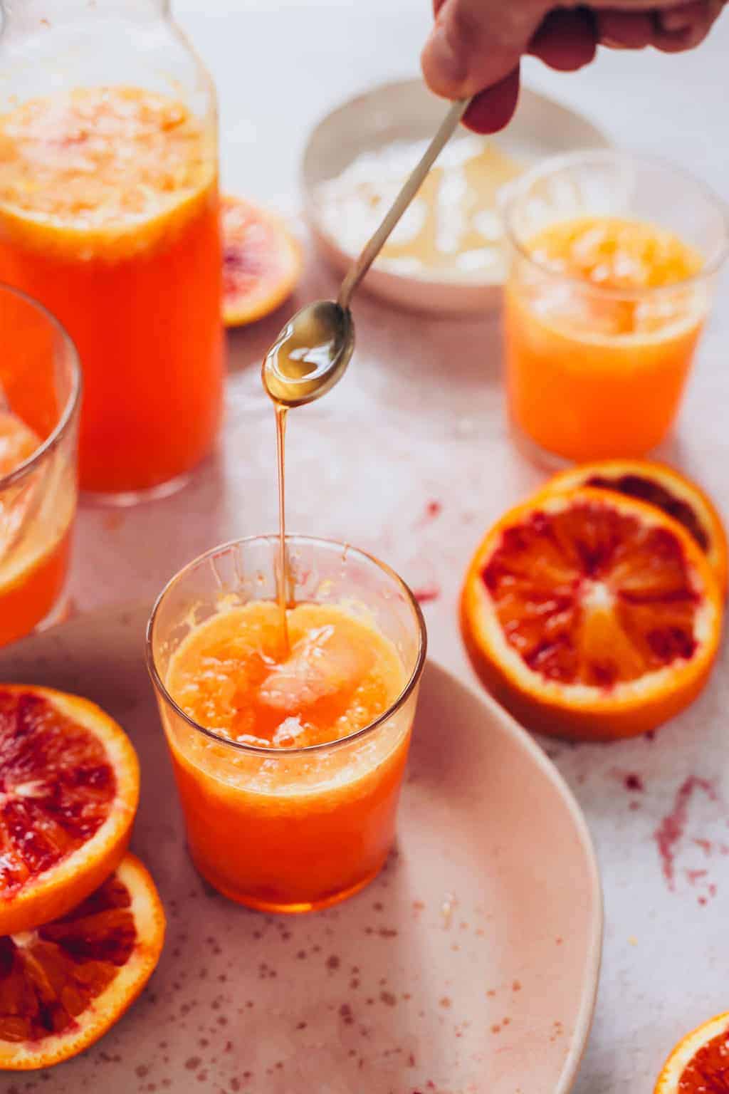 Blood orange sodas on a plate with honey going into the drink.