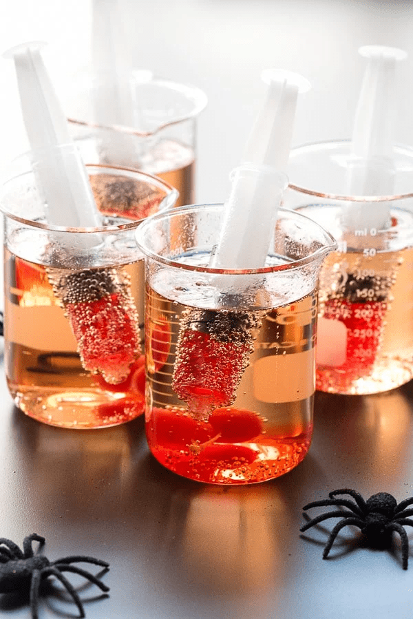 Halloween Shirley Temple served in a beaker with a syringe filled with red juice. 