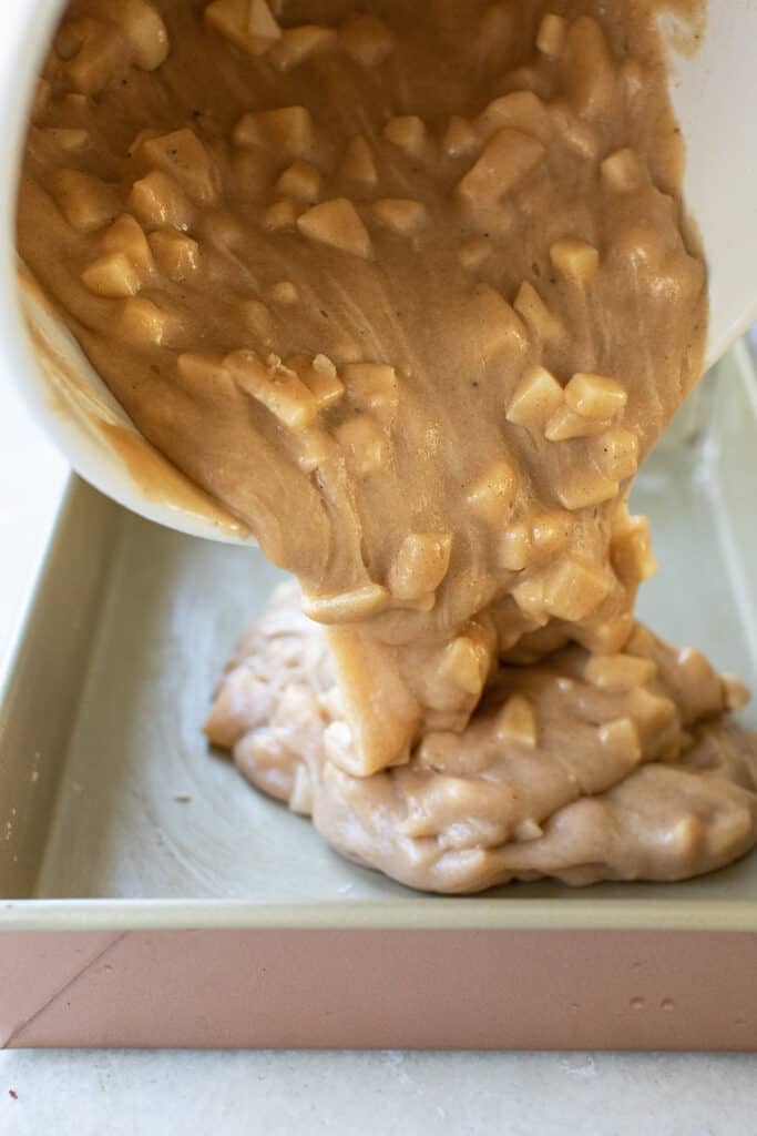 Pouring apple batter into a cake pan.