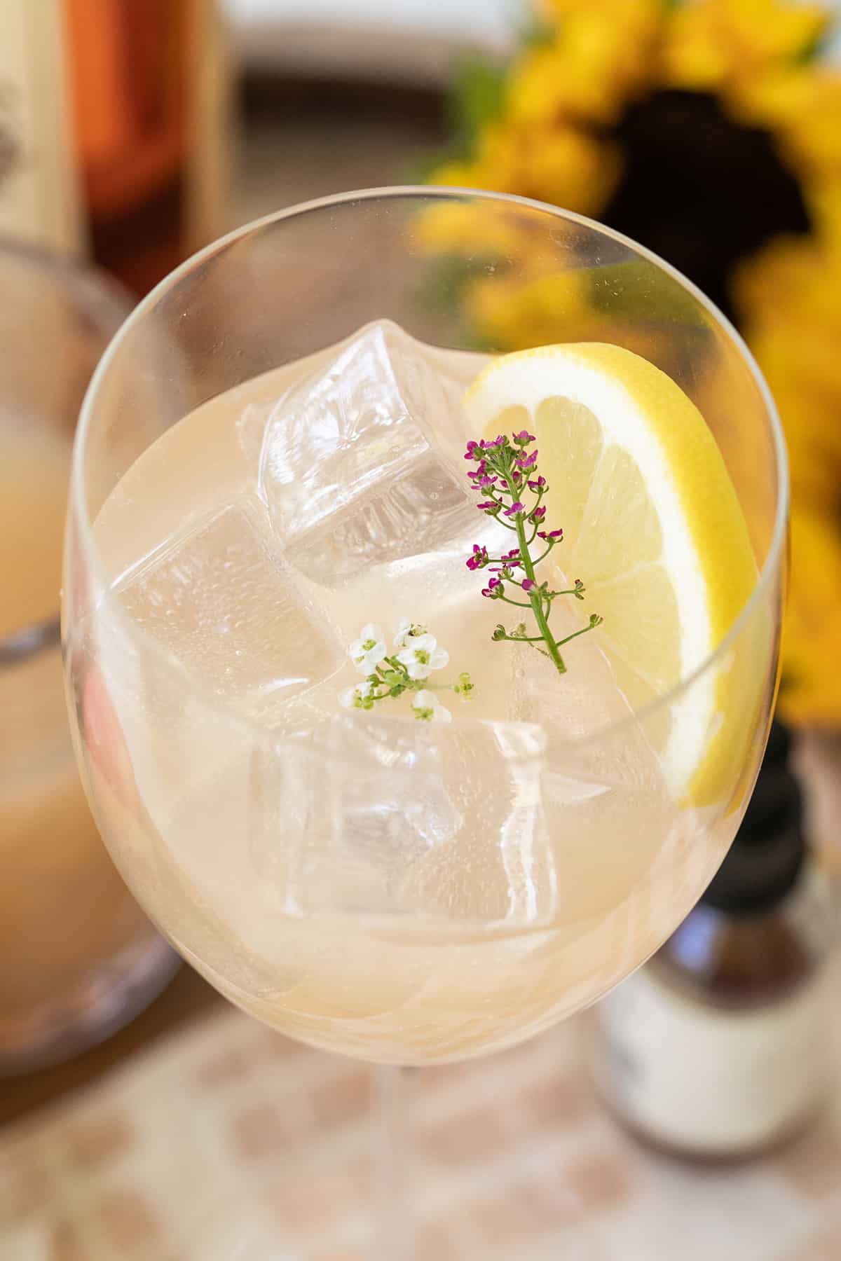 Cocktail made with apple cider and garnished with a lemon wedge and edible flower. 