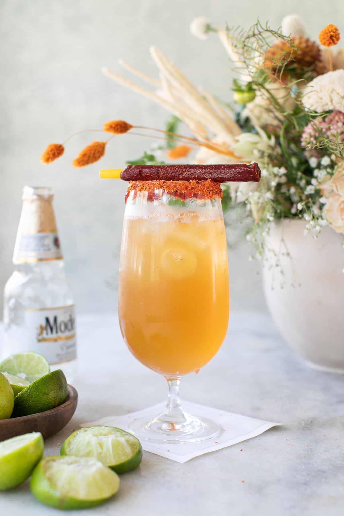 Michelada recipe in a glass with chammy stick and flowers.