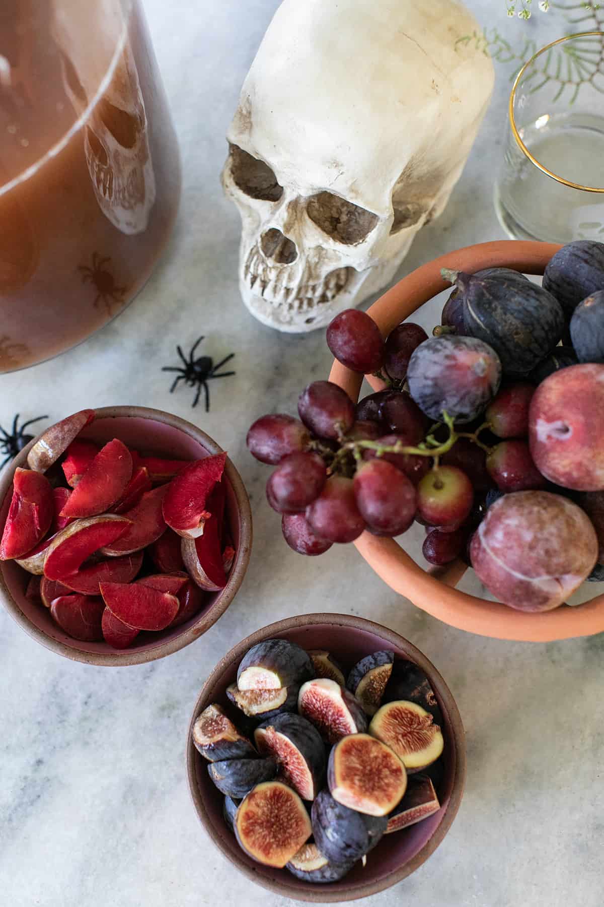 Figs, sliced plums and grapes in bowls with a skeleton.