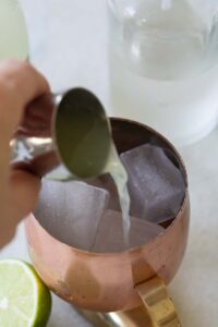 pouring lime juice into a copper mug.