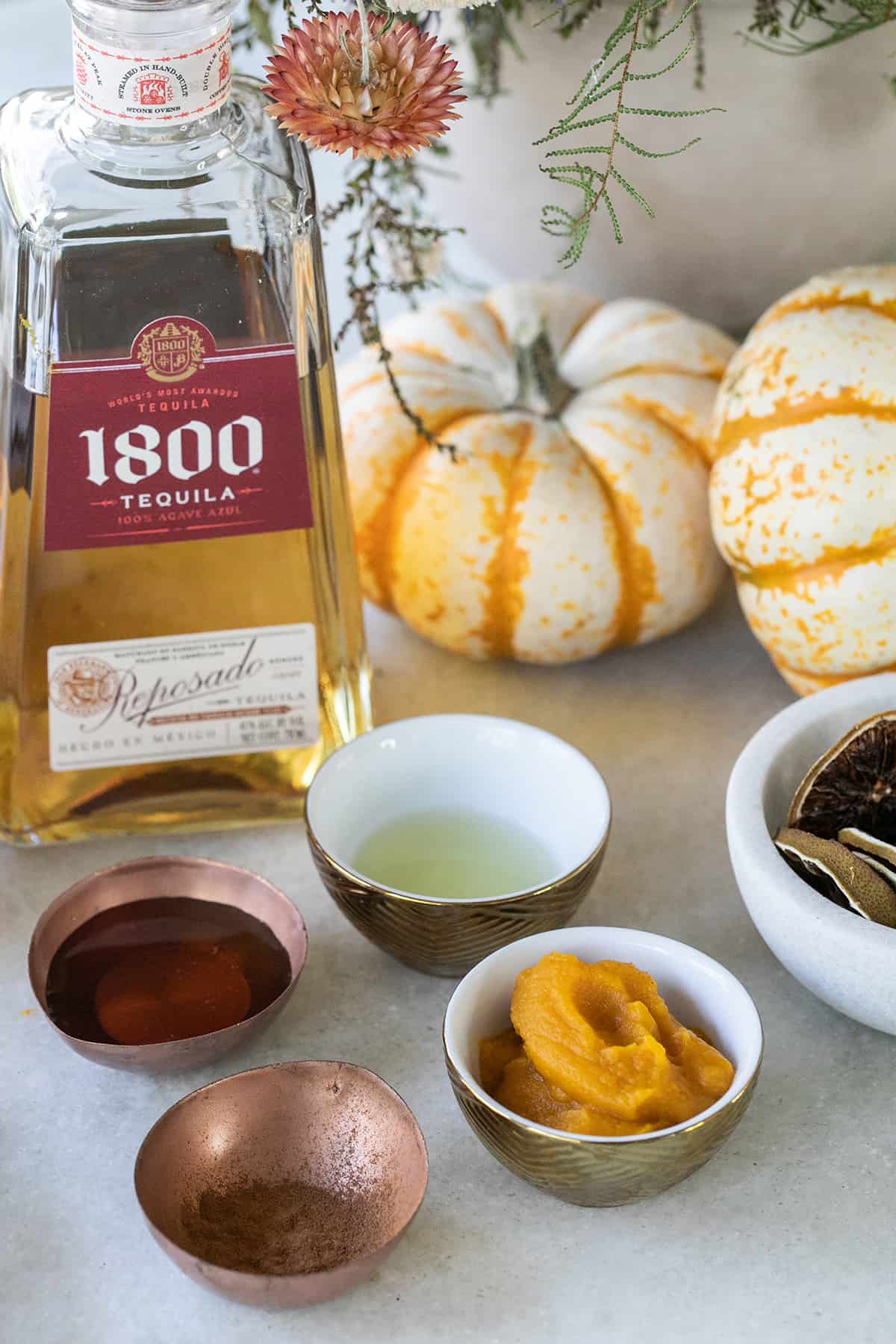 Pumpkin puree, maple syrup, lime juice and tequila in small bowls on a table.