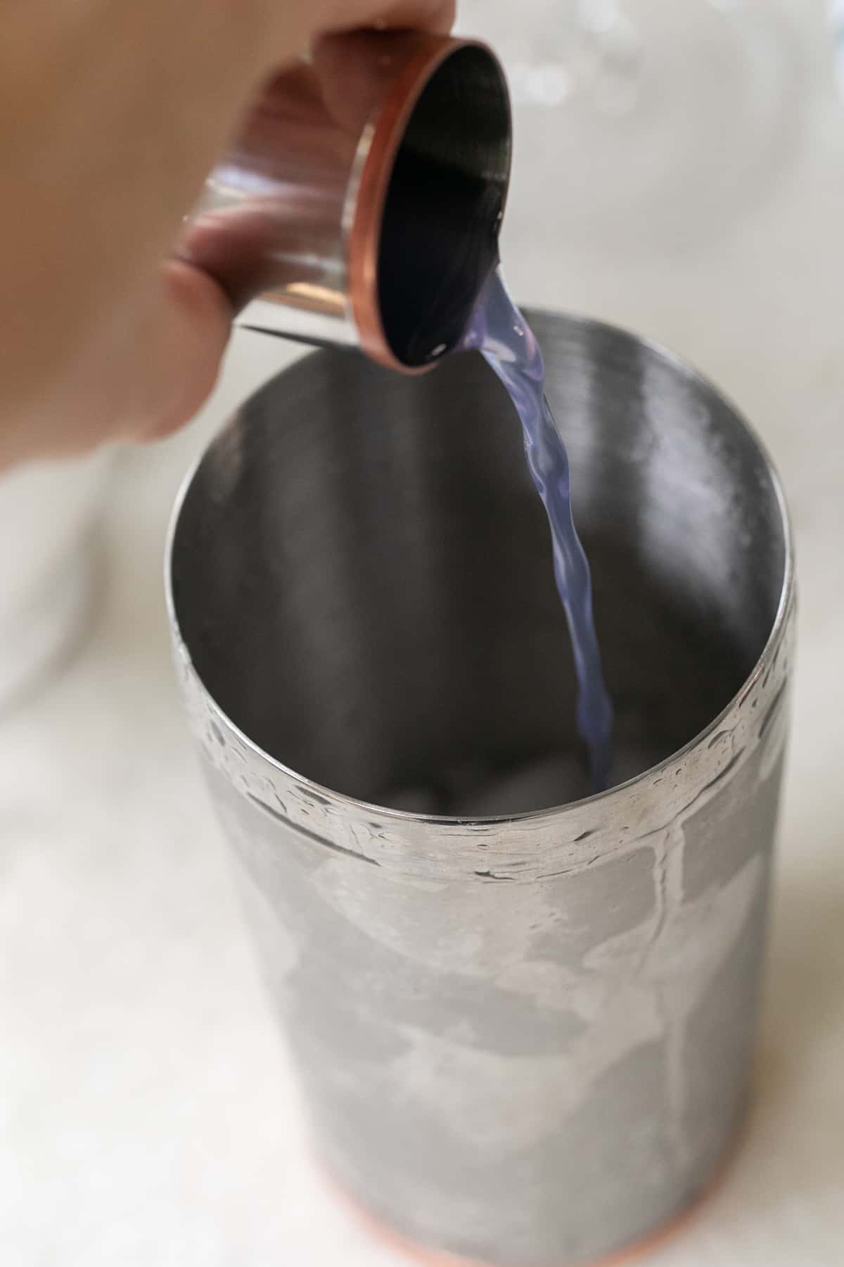 Pouring purple vodka into a cocktail shaker.