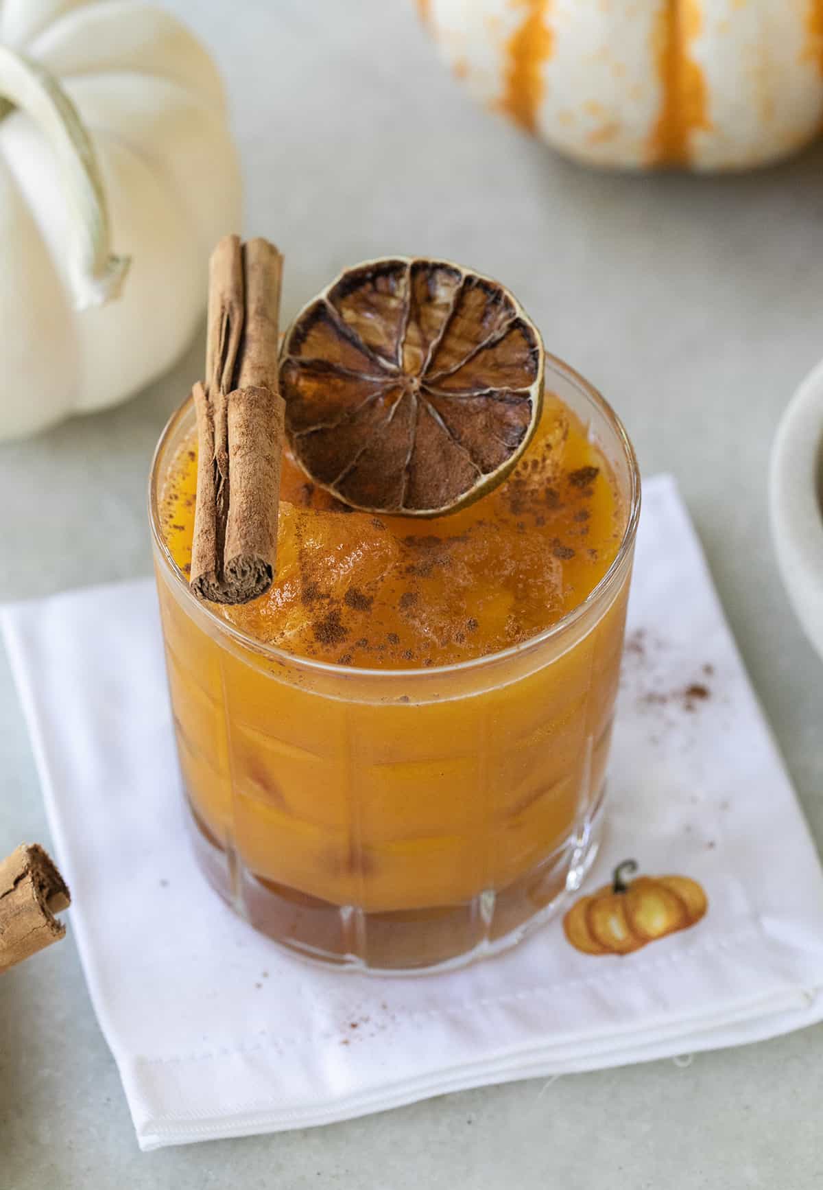 A fall margarita in a glass with a cute pumpkin napkin.