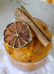 Cinnamon stick and a dehydrated lime wheel on an orange cocktail.