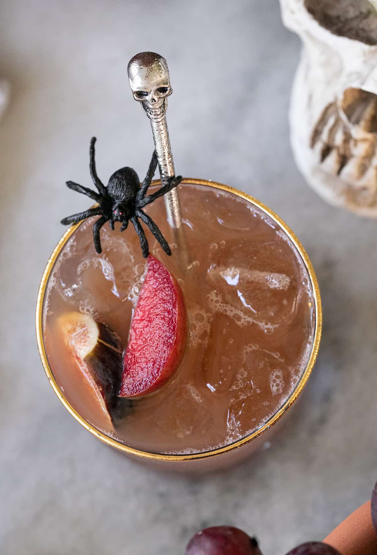 A glass filled with Halloween punch and fruit and with a fake spider on the glass.