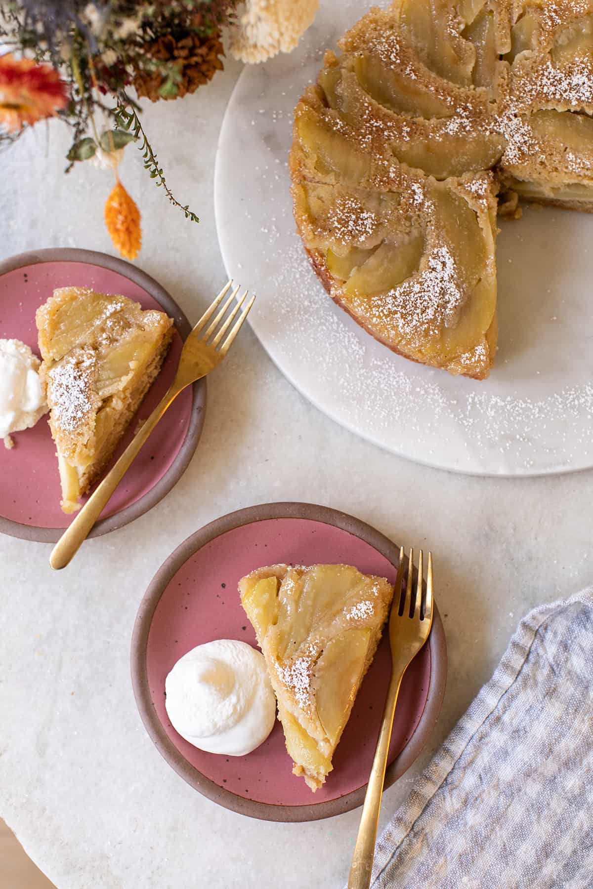 apple upside down cake on a pink plate with whipped cream. 