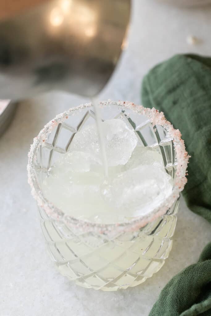 straining a mocktail into a glass filled with ice.