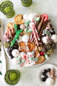 A Christmas dessert charcuterie board on a marble platter with green glasses.