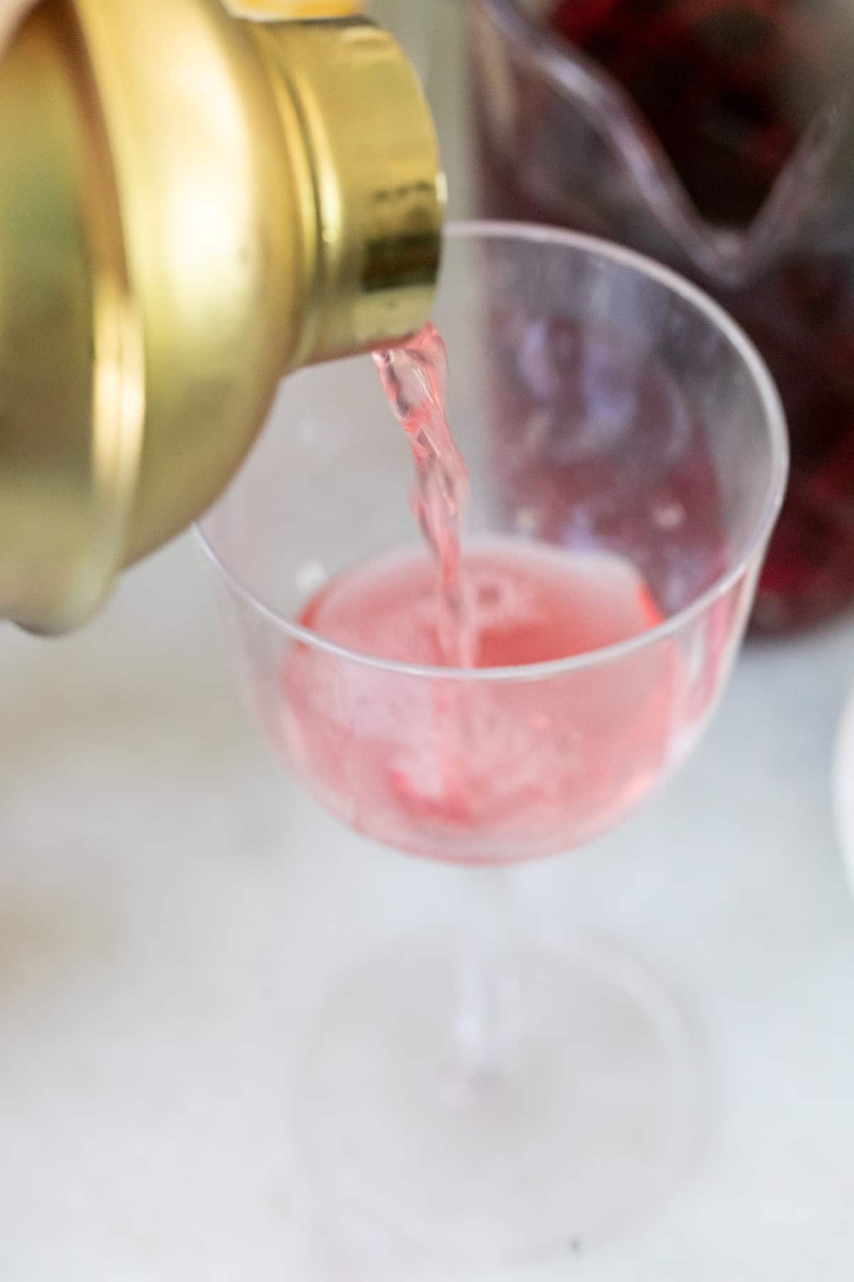 straining a red cocktail into a coupe glass.