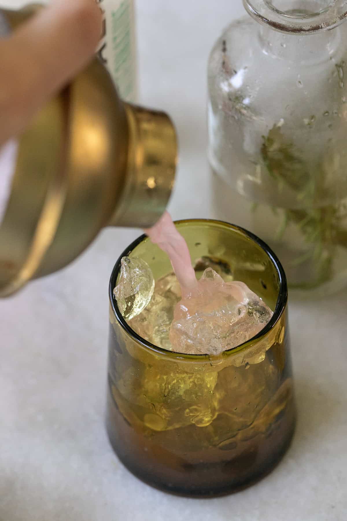 Pouring an apple cider mocktail into a green glass filled with ice.