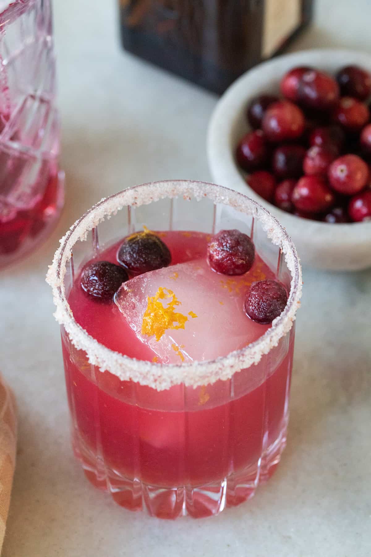 Cranberry margarita with a salted rim, orange zest and a large ice cube.