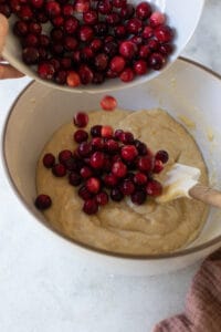 Pouring fresh cranberries into muffin batter.