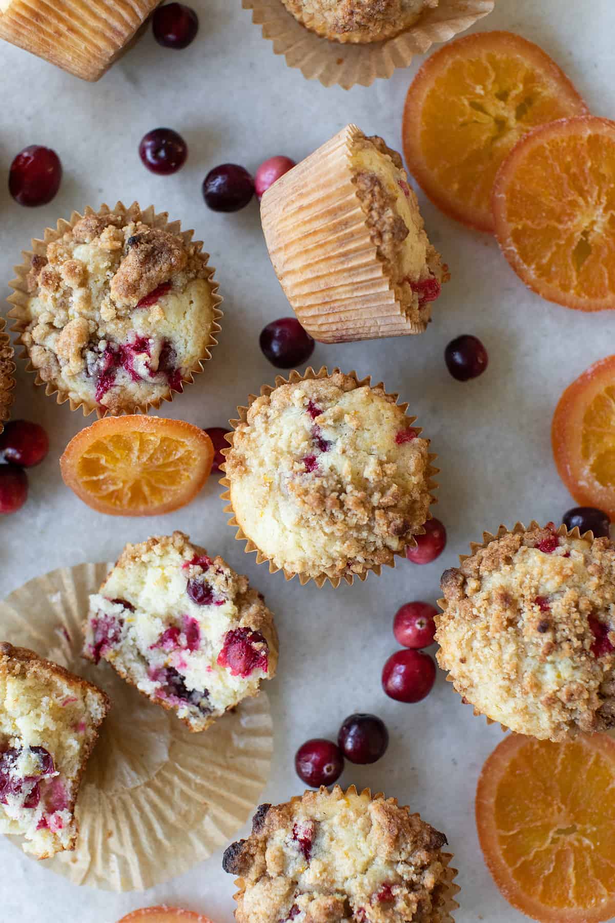 Orange cranberry muffins on a table with dried orange slices and fresh cranberries.