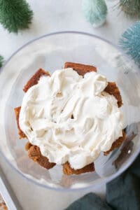 Layer of whipped cream over gingerbread cake in a trifle dish.