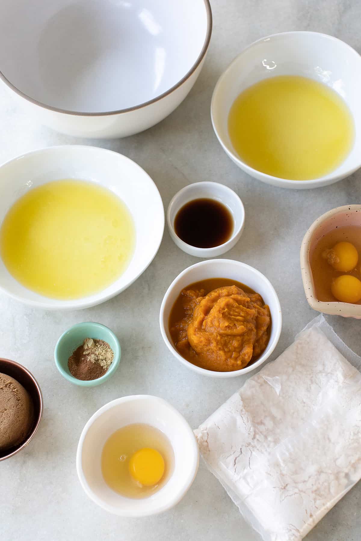 melted butter, eggs, cake mix,  ground spices, brown sugar and vanilla extract in small bowls on a table.