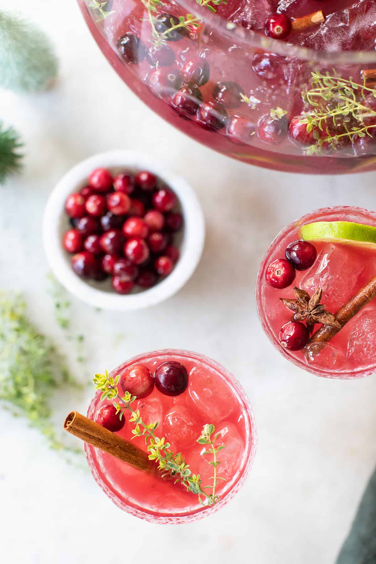 Glasses filled with red punch and cranberries garnished with cinnamon sticks and thyme.