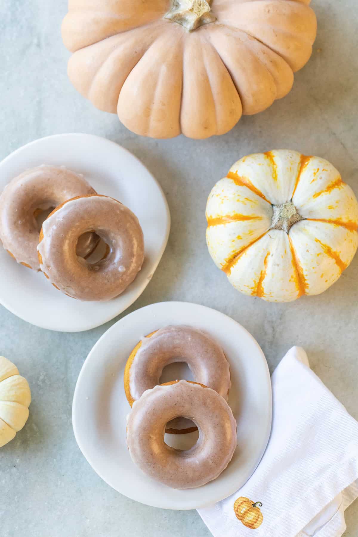 Four baked pumpkin donuts on white plates with two pumpkins.