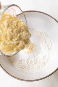 Pouring mashed bananas in a bowl with flour.