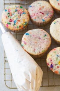 Homemade frosting in a piping bag next to confetti cupcakes.