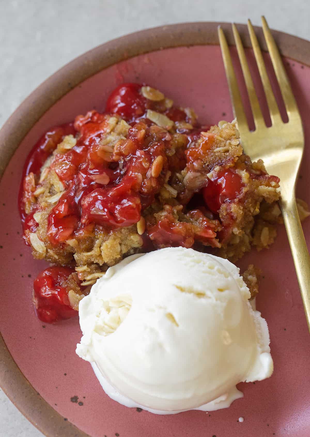 Cherry crisp on a pink plate with vanilla ice cream.