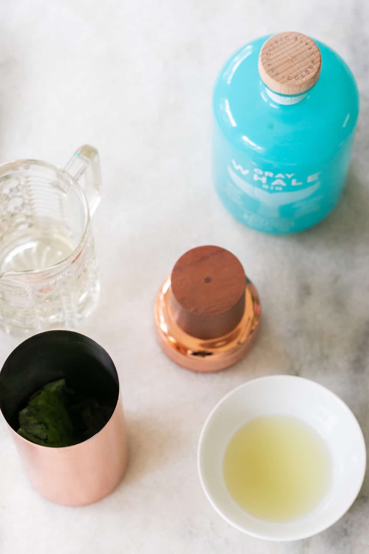 gin, lime juice, cocktail shaker and simple syrup on a table. 