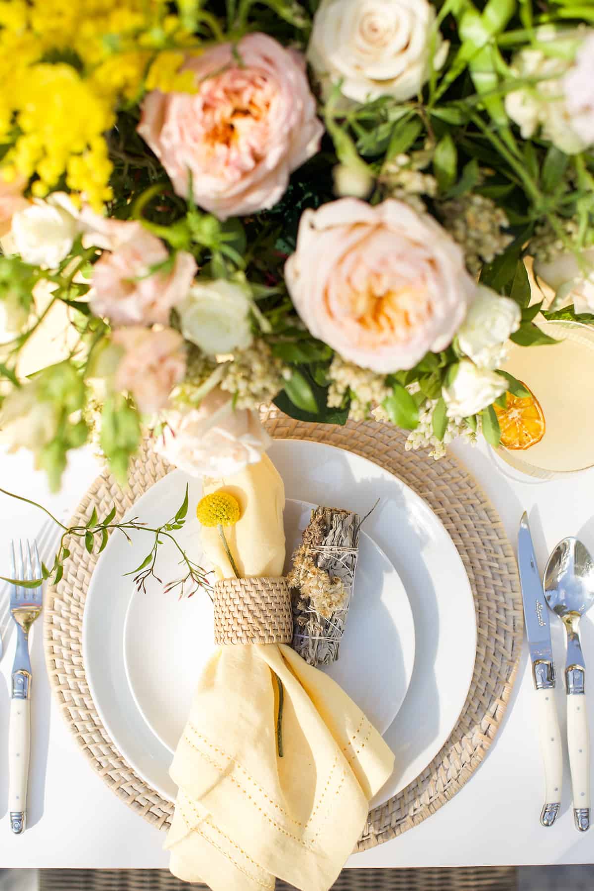 Table setting with yellow napkins, flowers and a properly set table.
