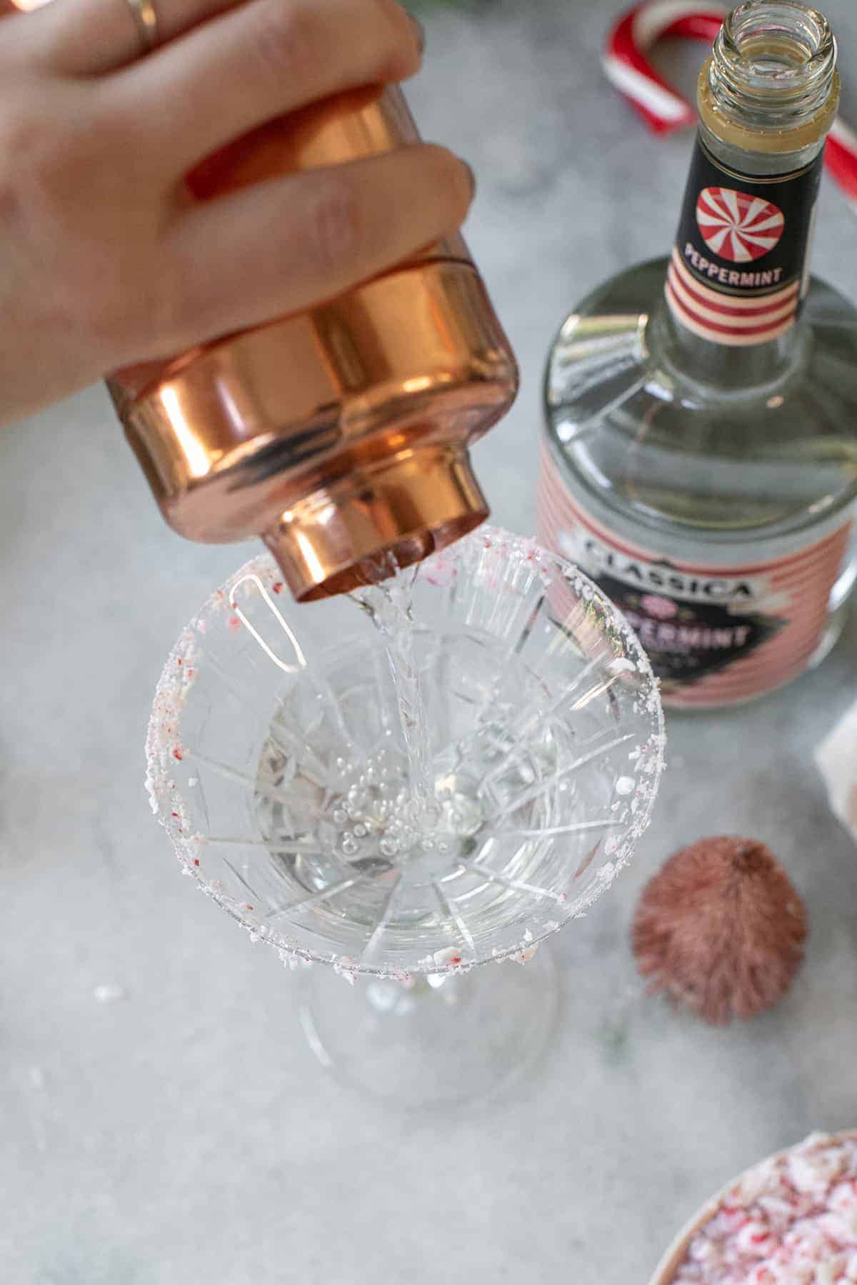 Pouring a peppermint martini into a glass.