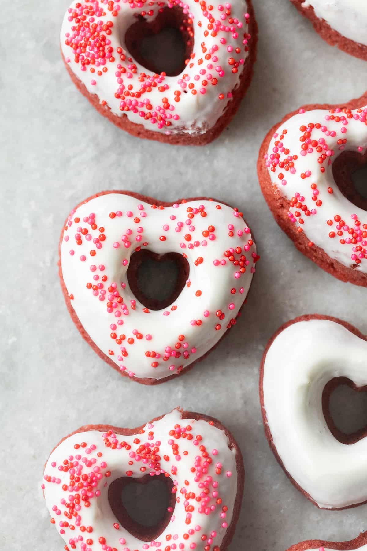 Heart-shaped baked red velvet donut with cream cheese glaze and sprinkles.