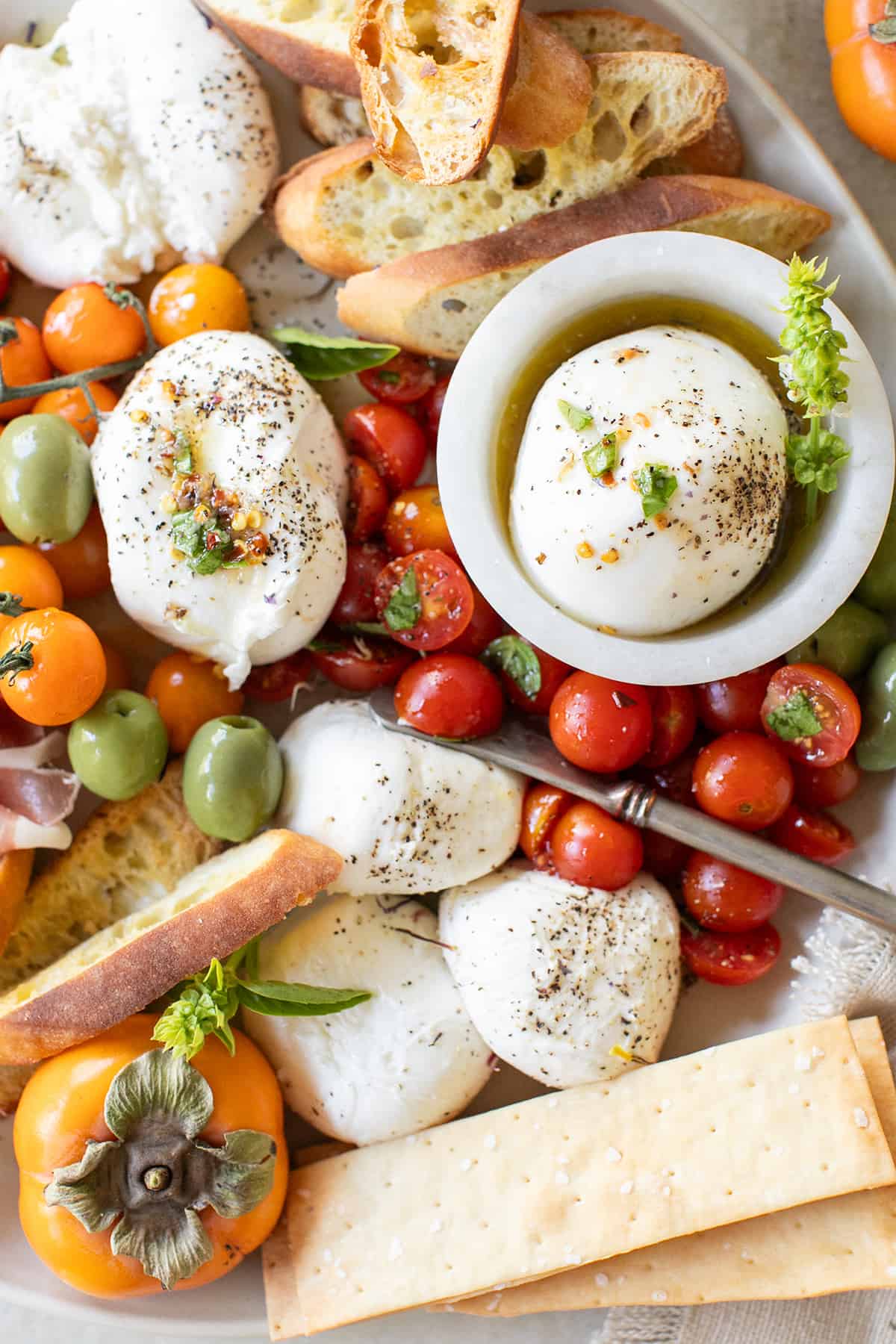 Burrata platter with fresh burrata, crackers, marinated cherry tomatoes, and olives.