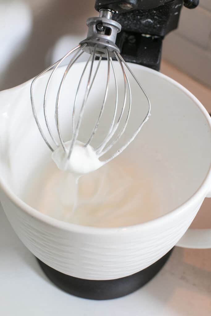 Egg whites being whipped in an electric mixer with the whisk attachment.
