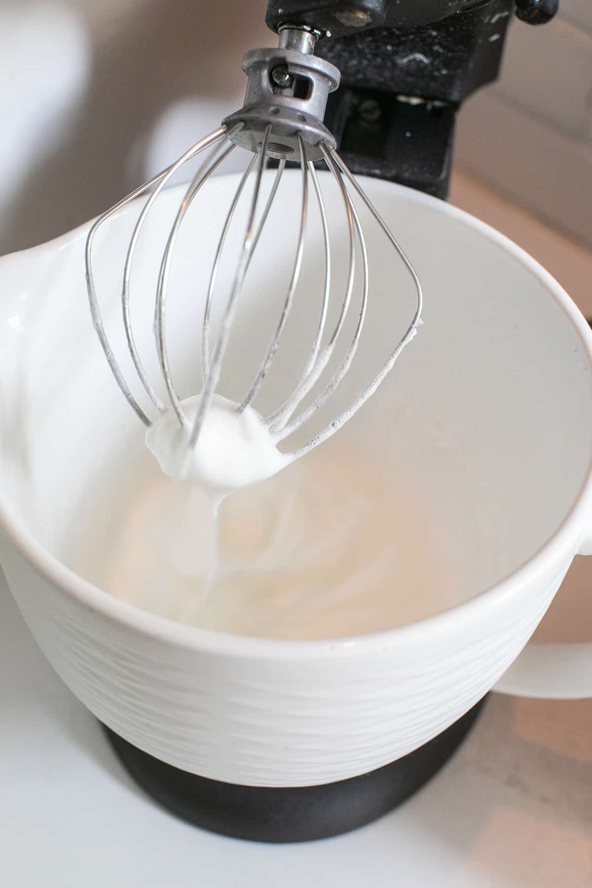 Egg whites being whipped in an electric mixer with the whisk attachment.