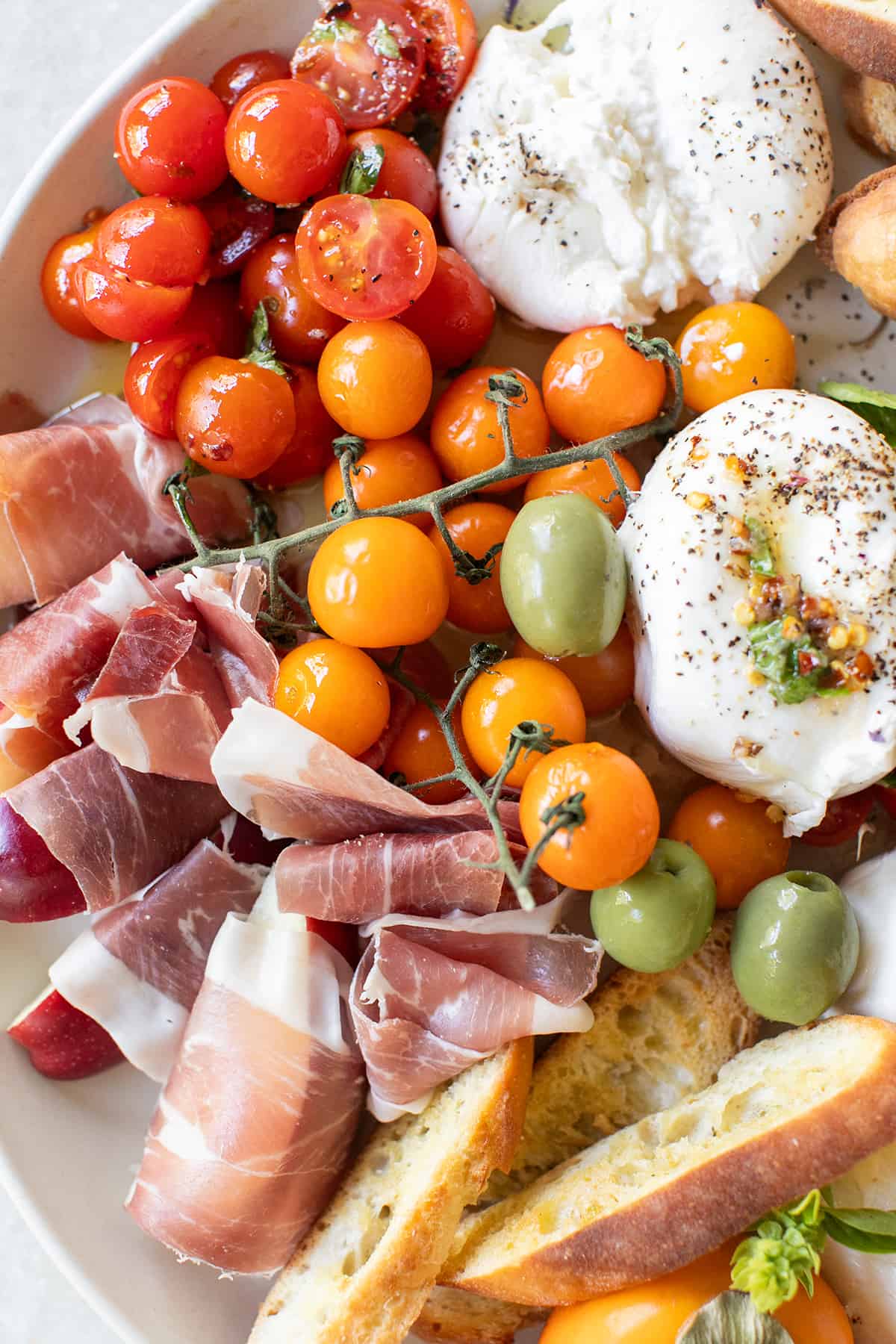 Easy burrata platter with crostini, crackers, fresh burrata, and fruit wrapped in prosciutto.