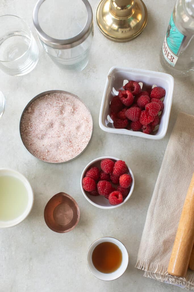 Tequila, raspberries, lime juice, salt, agave and tequila on a table.