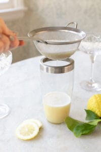 I am straining a lemon mixture into a cocktail shaker.