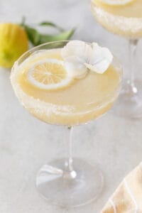 Lemon drink with flowers, whole lemon, and a sugared rim.